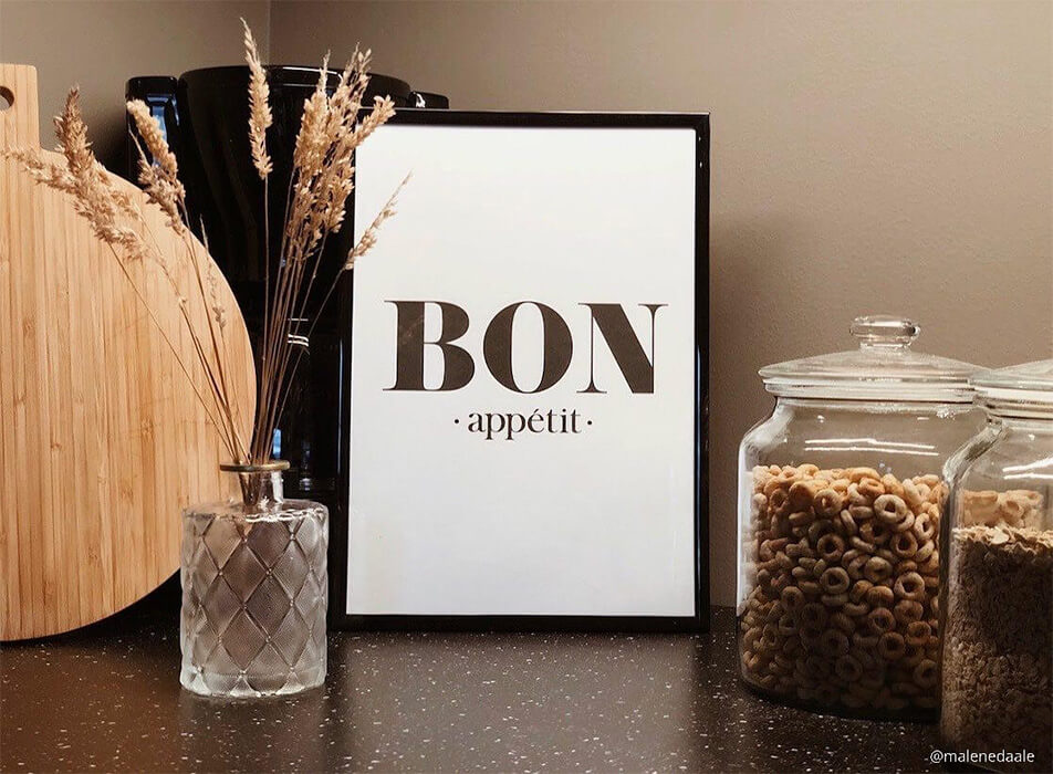 Keittiötaulu tekstillä Bon appétit, kahvinkeitin sekä lasipurkit tummalla työtasolla