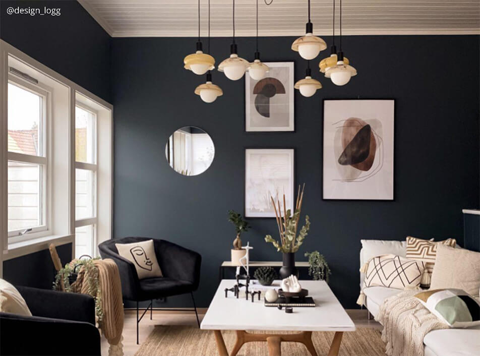 Olohuone tummilla seinillä, mustat samettinojatuolit, pyöreä peili, graafiset julisteet