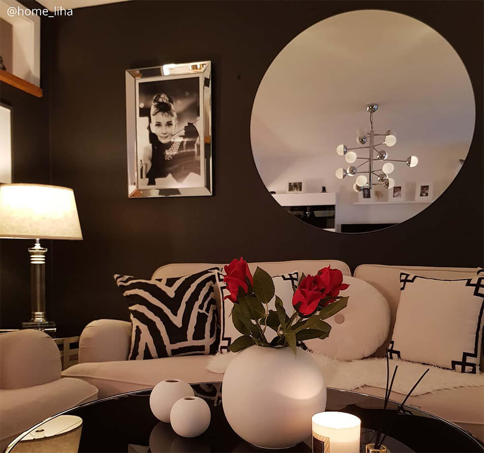 Olohuone tummasävyisellä seinällä, valkoinen sohva ja suuri, pyöreä peili